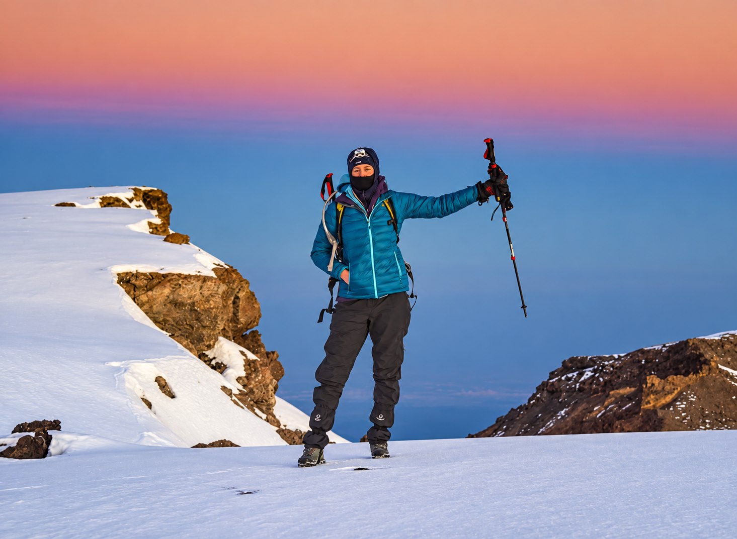 A climber celebrating on a snowy summit at sunrise