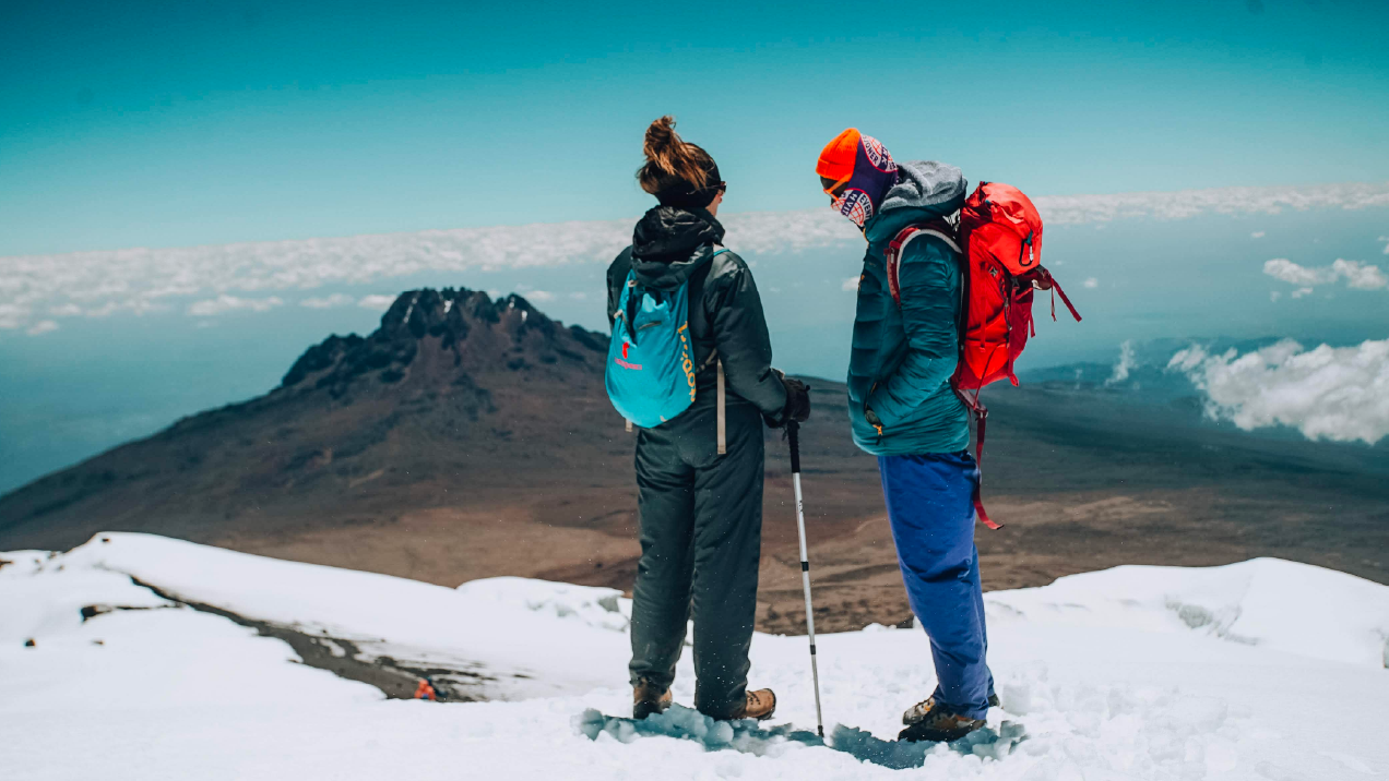 Two mountain climbers standing on a snowy ridge above the clouds
