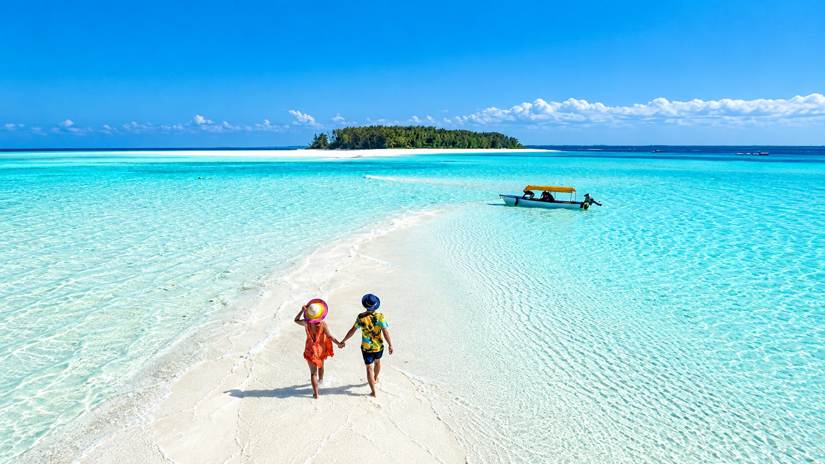 Two travellers walking hand in hand across a Zanzibar sandbar surrounded by turquoise water